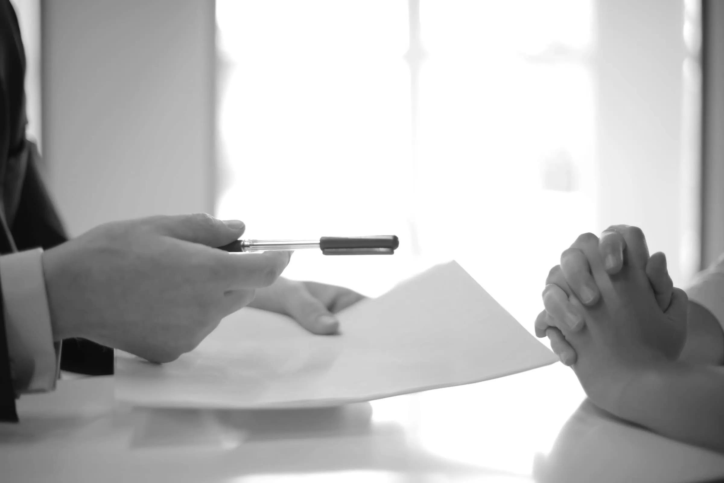 A document being handed across a table into window light