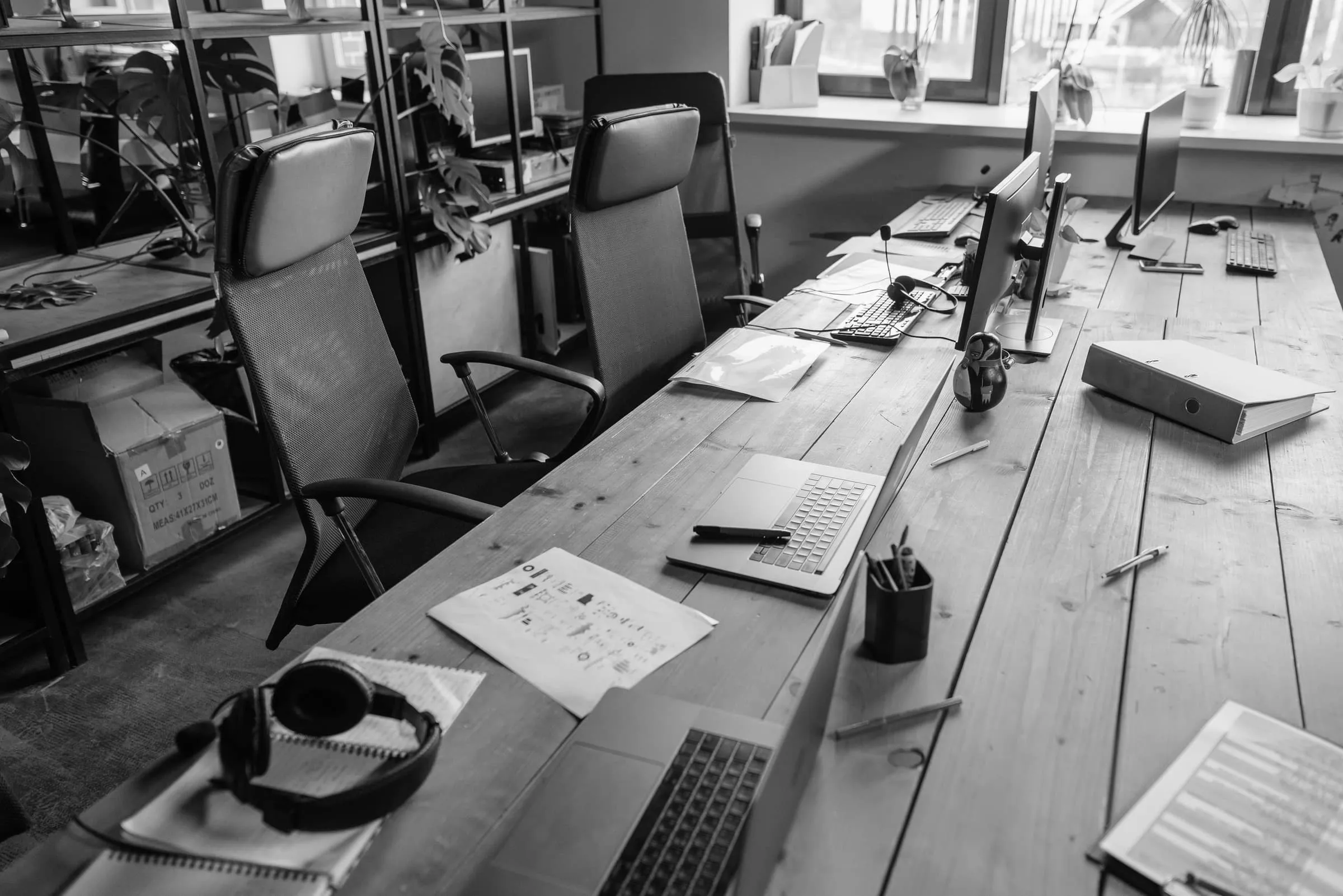 An empty shared office desk with laptops, papers and headphones left in place