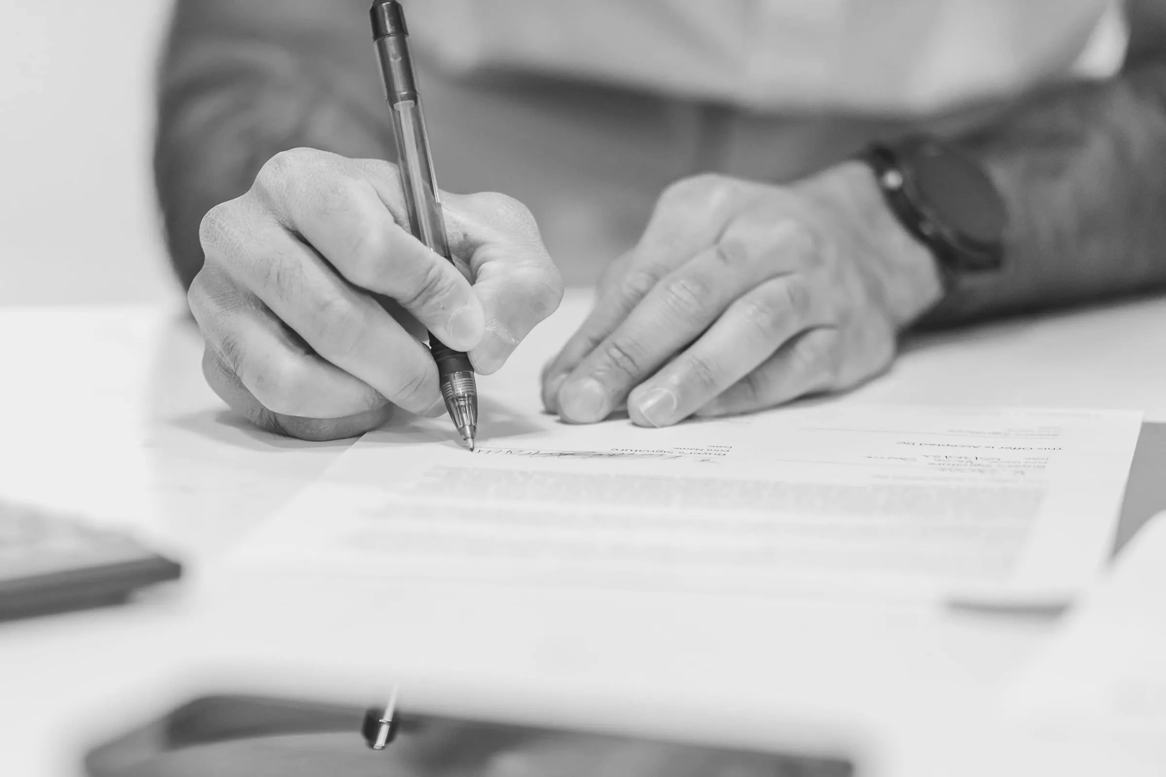 Two people at a desk, one signing a document while the other waits