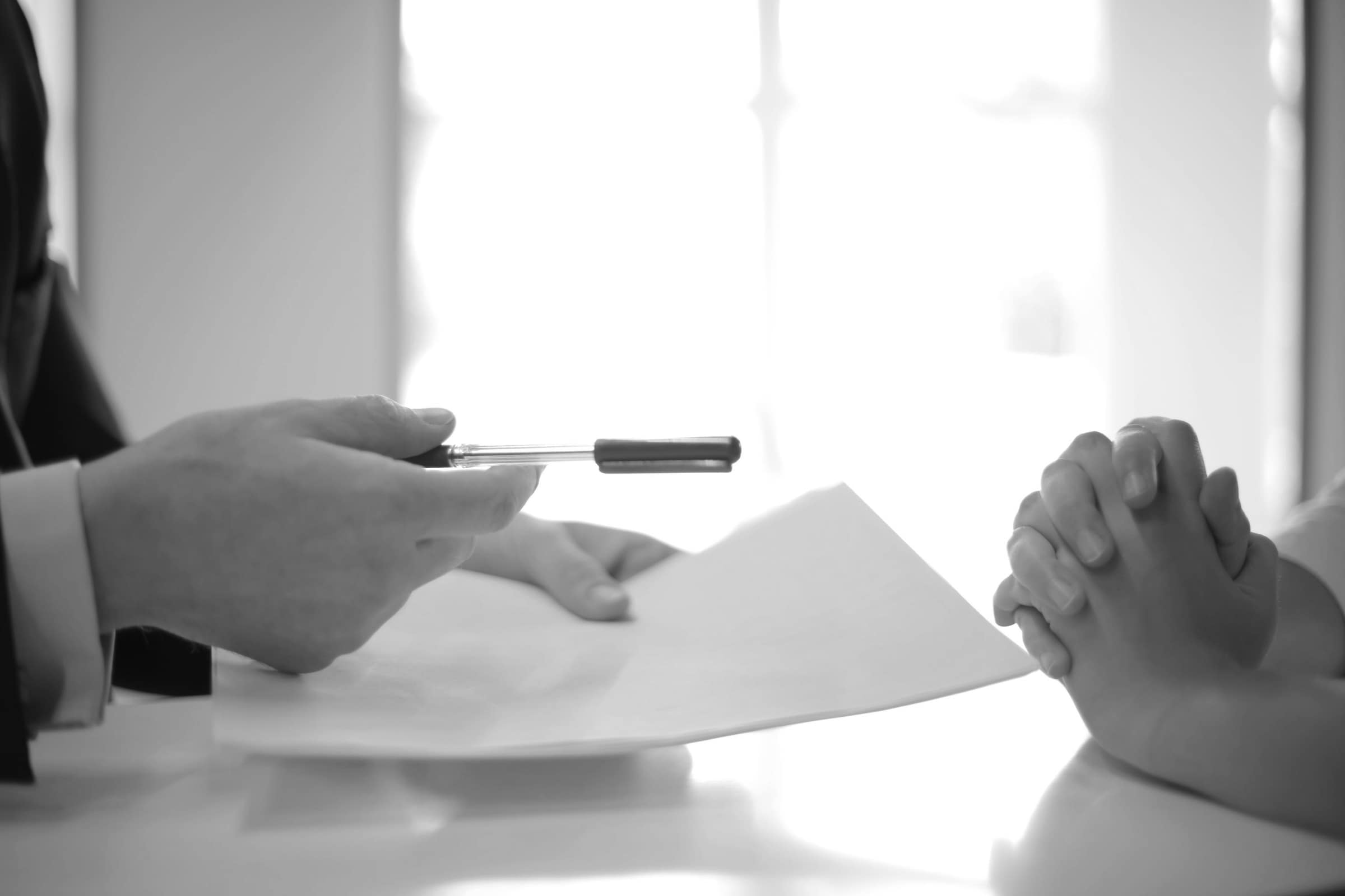 A document being handed across a table into window light